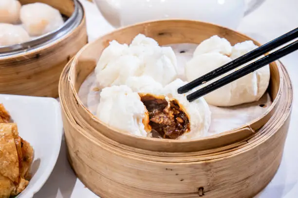 Photo of Delicious dim sum, famous cantonese food in asia - Fresh and hot Cha Siu Bao, BBQ pork bun in bamboo steamer in hong kong yumcha restaurant, close up