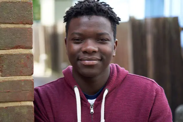 Photo of Portrait Of Smiling Teenage Boy Leaning Against Wall In Urban Setting