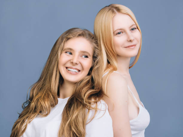 Close-up lifestyle friends portrait Two smiling girls in white T-shirts are standing shoulder to shoulder against the blue wall dearness stock pictures, royalty-free photos & images