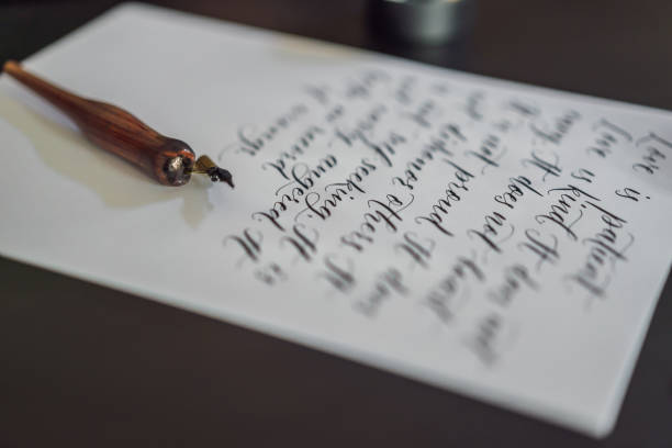 istock Calligrapher hands writes phrase on white paper. Bible phrase about love Inscribing ornamental decorated letters. Calligraphy, graphic design, lettering, handwriting, creation concept 1154998850