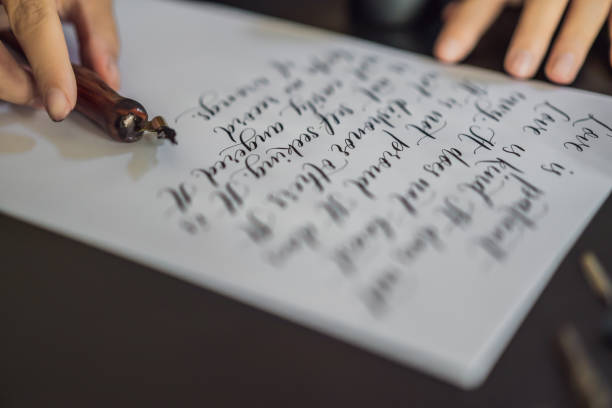 istock Calligrapher hands writes phrase on white paper. Bible phrase about love Inscribing ornamental decorated letters. Calligraphy, graphic design, lettering, handwriting, creation concept 1154999717
