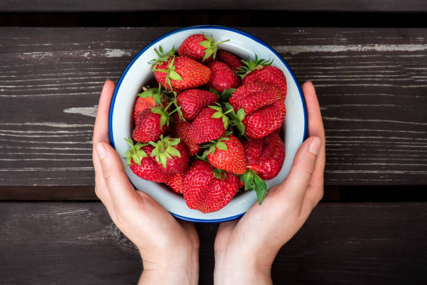 istock Female hands holding a plate with ripe red strawberries 1155001979