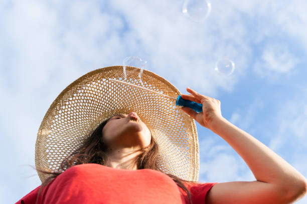 A Cheerful Young Adult happy to be outdoors, contemplating what surrounds her. Playing with bubbles. Close Up Shot. Happiness.