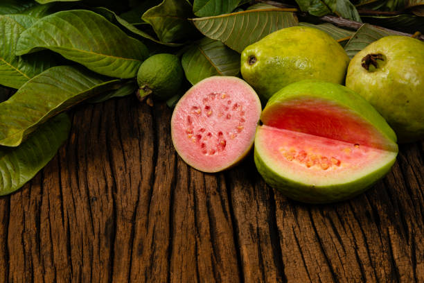 Fresh red guavas with green leaves on wooden demolition background. Wood texture and guava leaves Fresh red guavas with green leaves on wooden demolition background. Wood texture and guava leaves. guava photos stock pictures, royalty-free photos & images