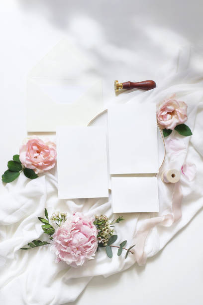 istock Feminine vertical wedding, birthday mock-up scene. Blank paper greeting cards, envelope, ucalyptus, pink roses, peony flowers on white table background. Light, shadow play. Flat lay, top view 1155010105