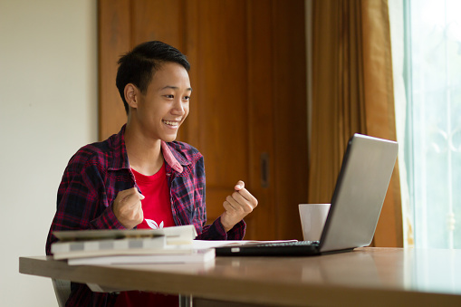 Happy teenage boy feeling excited to see a good news in email from laptop at home. online study, learning success, global education and e-leaning concept.