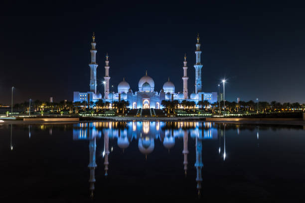 Iconic Islamic Site: Grand Mosque in Abu Dhabi, United Arab Emirates at night with a reflection in the pool showing off its beautiful colours of purple in the sky and water. stock photo