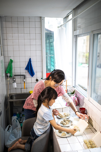 Taiwanese woman and her adorable daughter working together in the kitchen, serving Chinese dumplings on plate