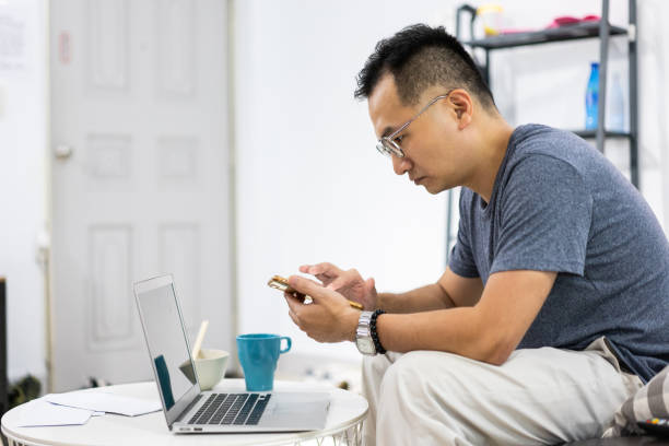 istock Mature man using laptop and phone at home 1155016189