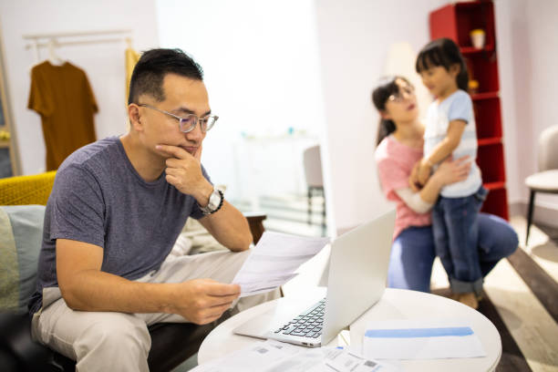 Worried man calculating bills while wife and daughter playing