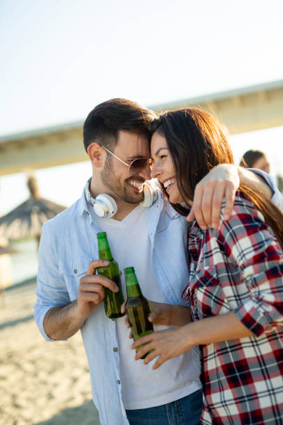 istock Happy couple smiling and drinking beer at beach 1155019070