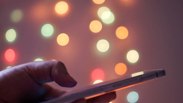 donna che tiene e usa il suo cellulare di notte e sfondo luce bokeh - business blurred motion text messaging defocused foto e immagini stock