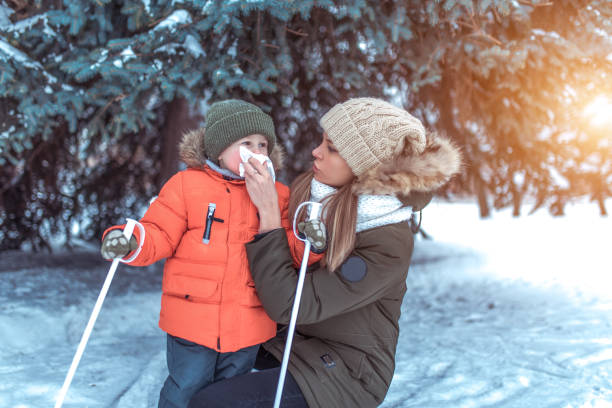 eine frau mama wischt ihre nase mit taschentuch, schnauze serviette kleines kind, fürsorgliches kind während der kalten jahreszeit im winter draußen, hintergrund schneewehen von weihnachtsbaum. ein kleiner junge ist 3-4 jahre alt. - 3 4 years cute beauty beautiful stock-fotos und bilder