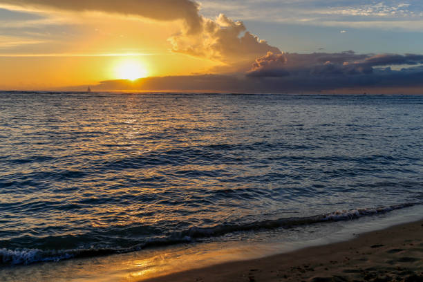 istock Bright yellow sun setting with small waves on sandy beach with room for text 1155029069