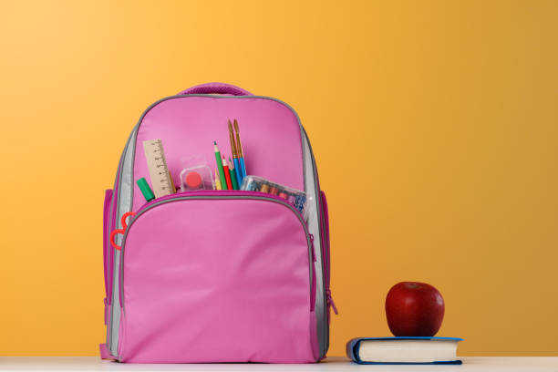 istock Student set. Pink backpack with office supplies, a book, a red apple on the table on a yellow background. Back to school. 1155031640