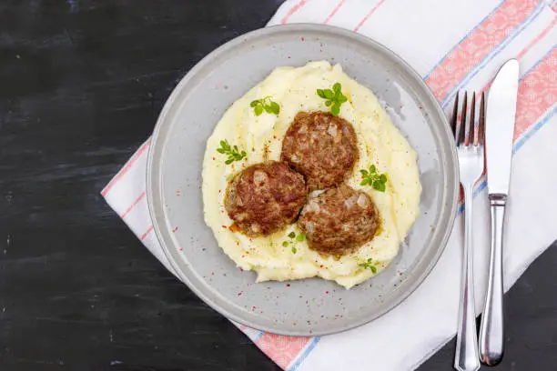 Mashed potatoes and meat balls on gray plate, decorated with fresh basil