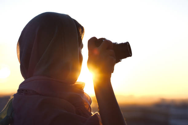 Arab Woman Photographer in a scarf taking picture using Camera on the sunset background. Halal travel concept Arab Woman Photographer in a scarf taking picture using Camera on the sunset background. Halal travel concept muslim photographer stock pictures, royalty-free photos & images