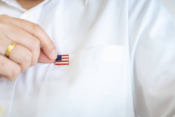 nahaufnahme der hand des mannes hält united state of america nation flagge pin auf weißen hemden flagge. - patriotism usa flag jewelry stock-fotos und bilder