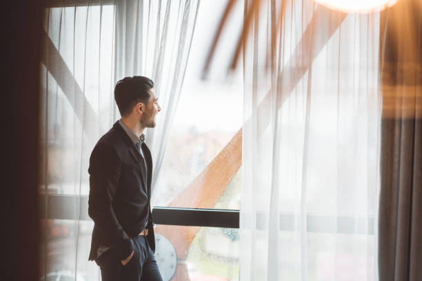 istock A young man in a suit looking through the window and smiling 1155044491