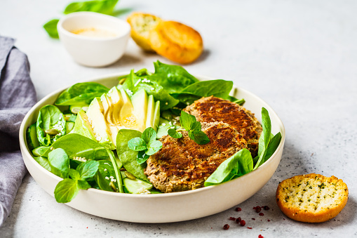 Green salad with avocado, cucumber and lentil cutlet in a white plate.