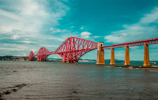 A train travels across the forthbridge on a sunny afternoon