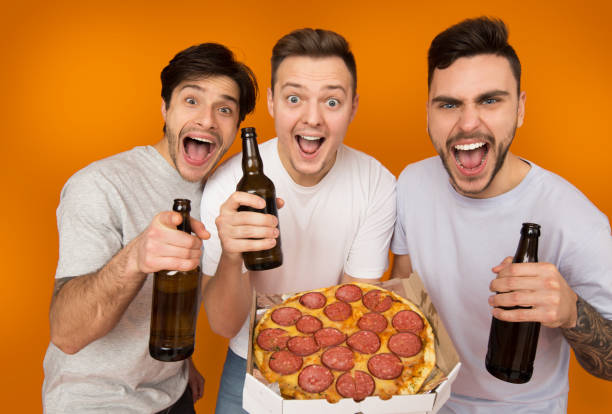 istock Happy friends drinking beer and eating pizza, orange background 1155046404