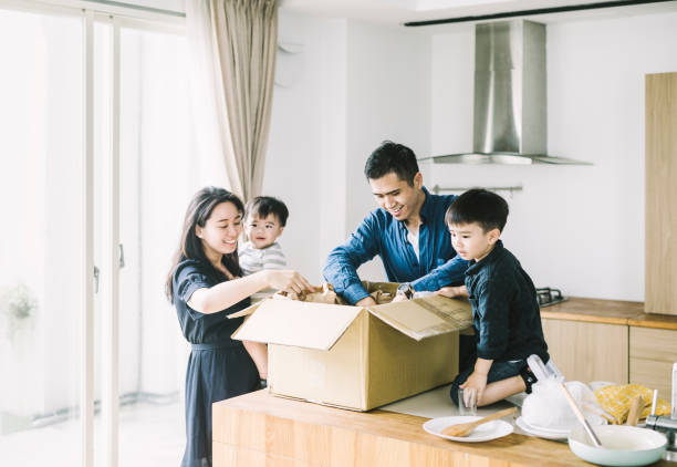 happy parents with sons unpacking cardboard box - asian ethnicity child four people couple imagens e fotografias de stock