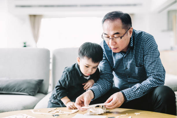 Grandfather making airplane toy for cute grandson Grandfather assembling model airplane for cute grandson. Mature man is assisting boy in making toy. They are in living room. child candid indoors lifestyles stock pictures, royalty-free photos & images