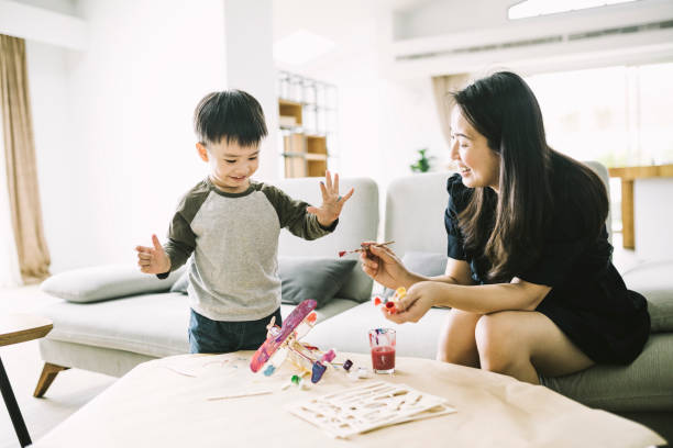 istock Smiling mother painting model airplane for son 1155050742
