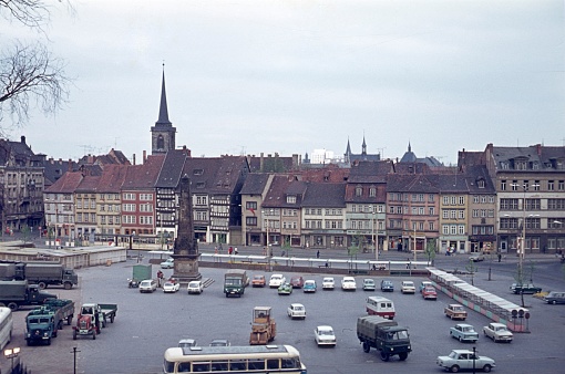 Erfurt, Thuringia, Germany, 1975. The cathedral square of Erfurt with old half-timbered houses, vehicles and market stalls.