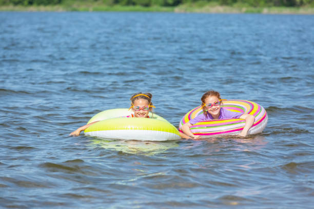 две девушки, плавающие во внутренней трубе плавать игрушки на озере - inner tube swimming lake water стоковые фото и изображения