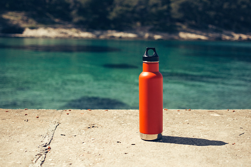 An insulated orange water bottle at the beach