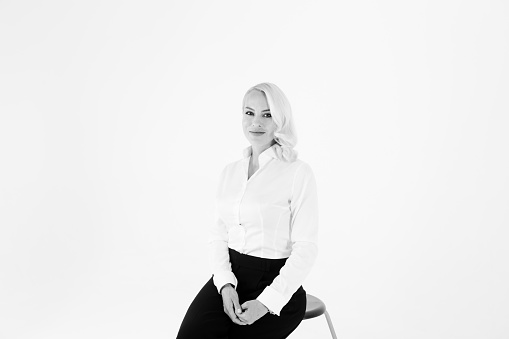 Studio portrait of a beautiful blonde woman in a white shirt and black pants against white plain background