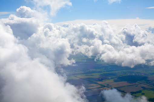 White clouds on blue sky background above green land, cumulus clouds high in skies, beautiful cloudy landscape view from plane, earth covered with clouds on sunny summer day, flight by airplane view