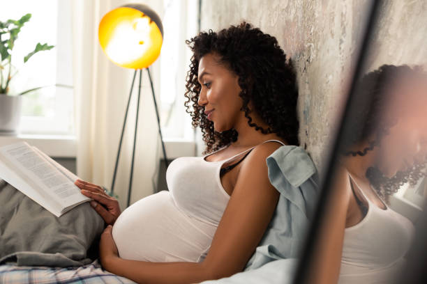 istock Expectant mother with a book reclining on her bed. 1155061293