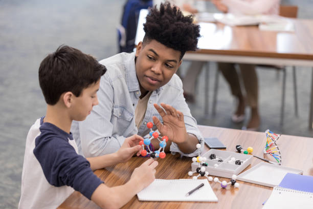 istock Young adult man lets elementary school boy use molecular model 1155064202