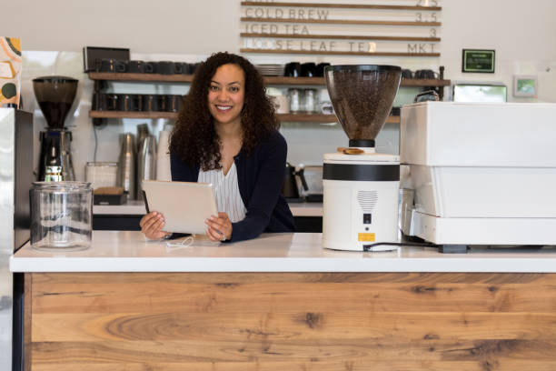 istock Coffee shop employee holding digital tablet looks at camera 1155064303