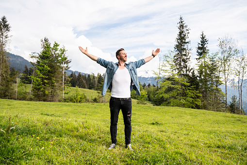 Handsome man is standing in the mountains with his arms wide open. Concept: back to nature, simple life