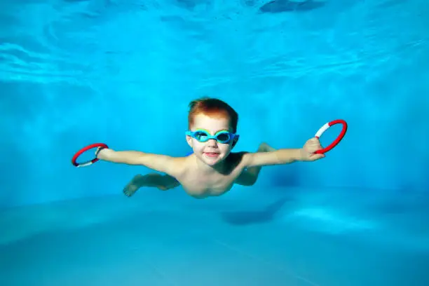 Sporty little boy swimming underwater in the pool with toys in his hands. Portrait. Close up. Underwater photography. Horizontal orientation.