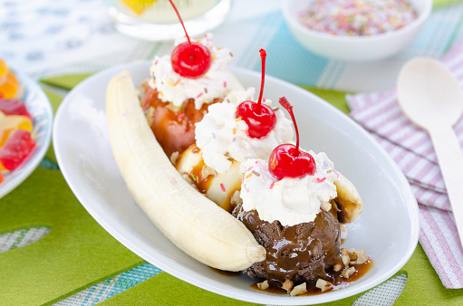 Homemade banana split served for a delicious treat with scoops of vanilla, strawberry and chocolate, drizzled with caramel sauce, nuts, sprinkles,topped with whipped cream and garnished with Maraschino cherries.