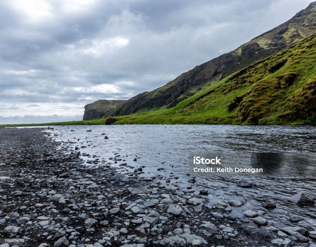 Stream of water with mountain and moody sky in background beside Scogafoss waterfall, Iceland Stream of water with mountain and moody sky in background near Scogafoss waterfall, Iceland Adventure Stock Photo