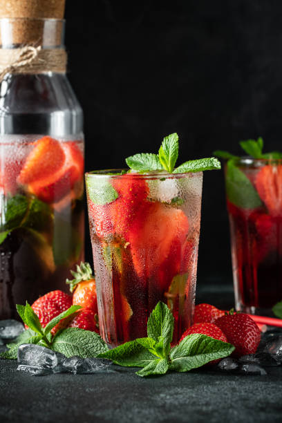 istock Fresh lemonade with ice, mint and strawberry on top in glass on black table background. Cold summer drink. Sparkling glasses with berry cocktail 1155076062