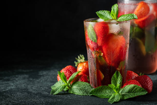 istock Fresh lemonade with ice, mint and strawberry on top in glass on black table background, copy space. Cold summer drink. Sparkling glasses with berry cocktail 1155076067