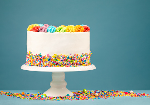 White Birthday cake with rainbow icing and colorful Sprinkles over a blue background.