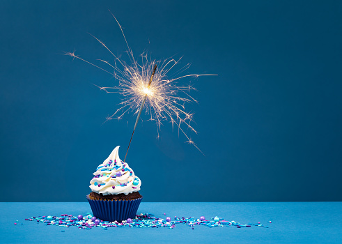Birthday Cupcake with sparkler against a blue background.