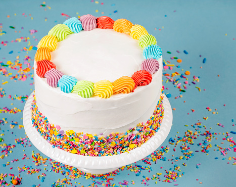 Birthday cake with rainbow icing and colorful Sprinkles over a blue background.