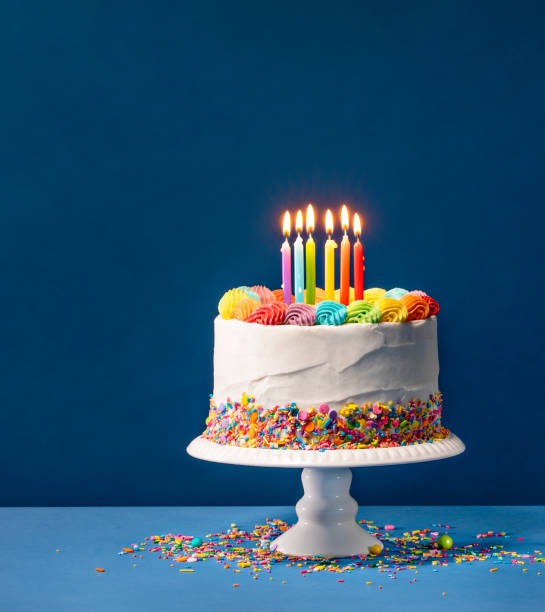 Colorful Birthday Cake over Blue Birthday cake with rainbow icing, colorful Sprinkles and lit candles over a blue background. birthday cake stock pictures, royalty-free photos & images