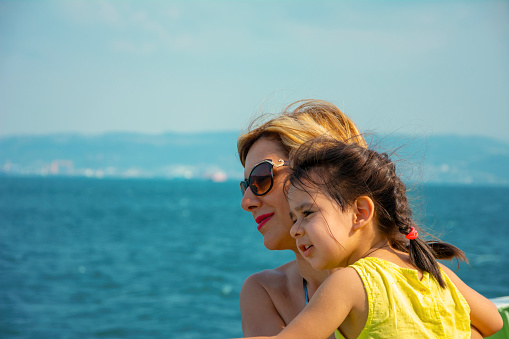 Little girl in her mother's lap, mother hugged her daughter, sun glasses, baby, daughter,  sea, view
