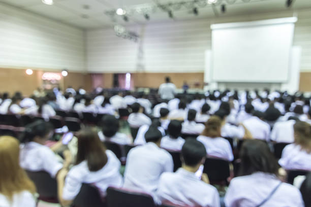 istock Blurred abstract background of educational conference in auditorium hall with students sitting in seat rows and presenters on stage 1155089058