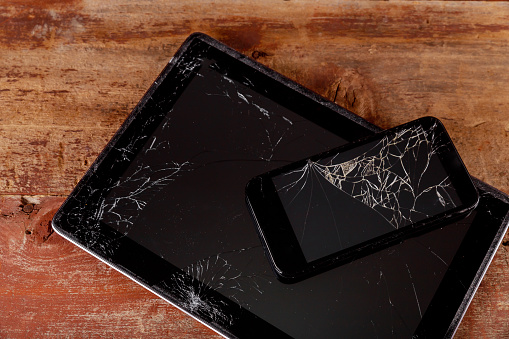 Broken tablet and smart phone touch screen electronic device on wooden background.